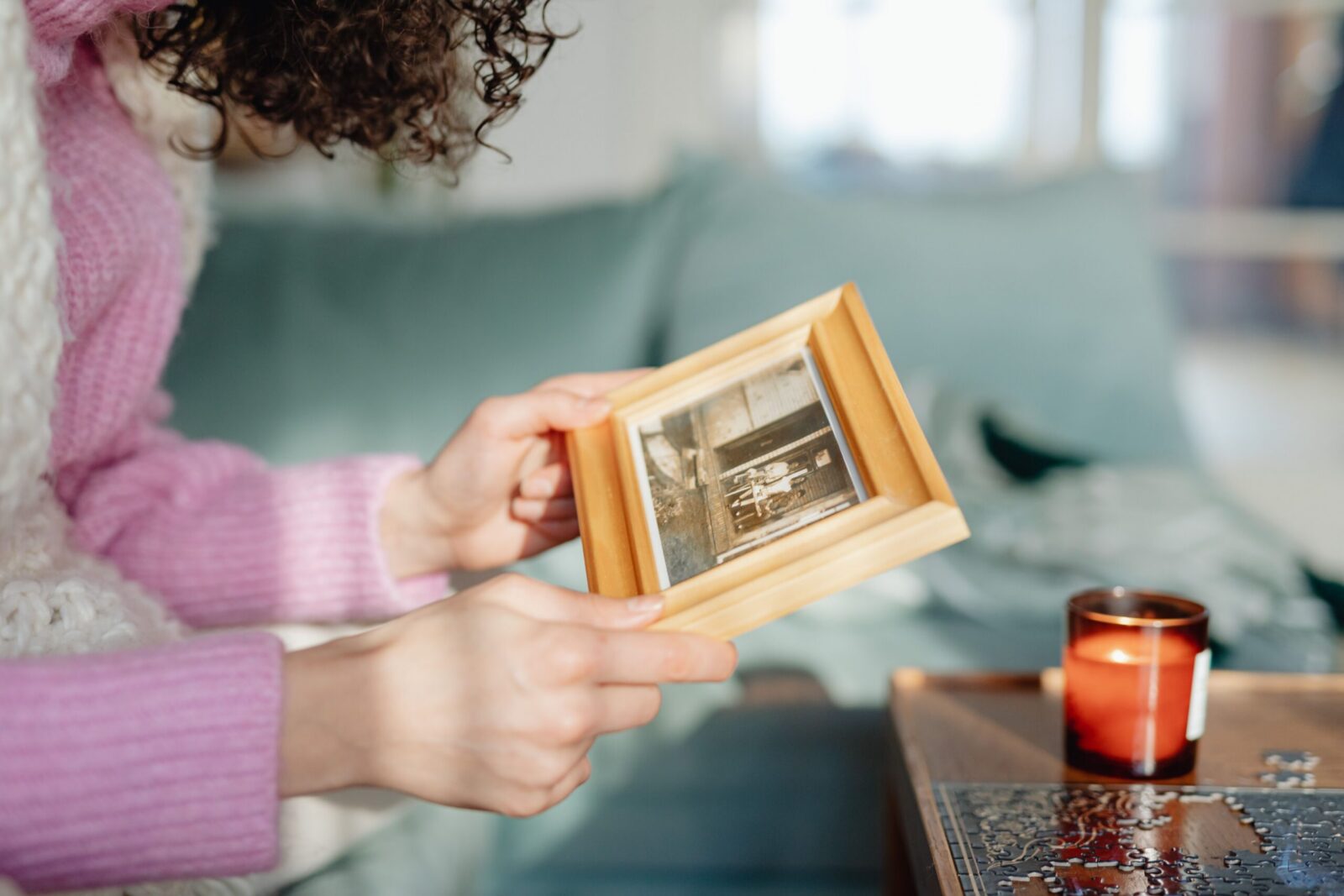A person in a pink sweater holding a picture frame indoors, near a candle.