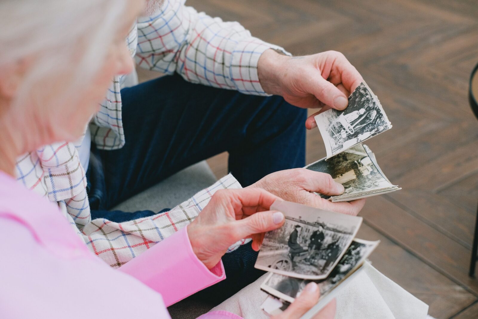 Elderly couple reminiscing over vintage black and white photographs, exploring memories.